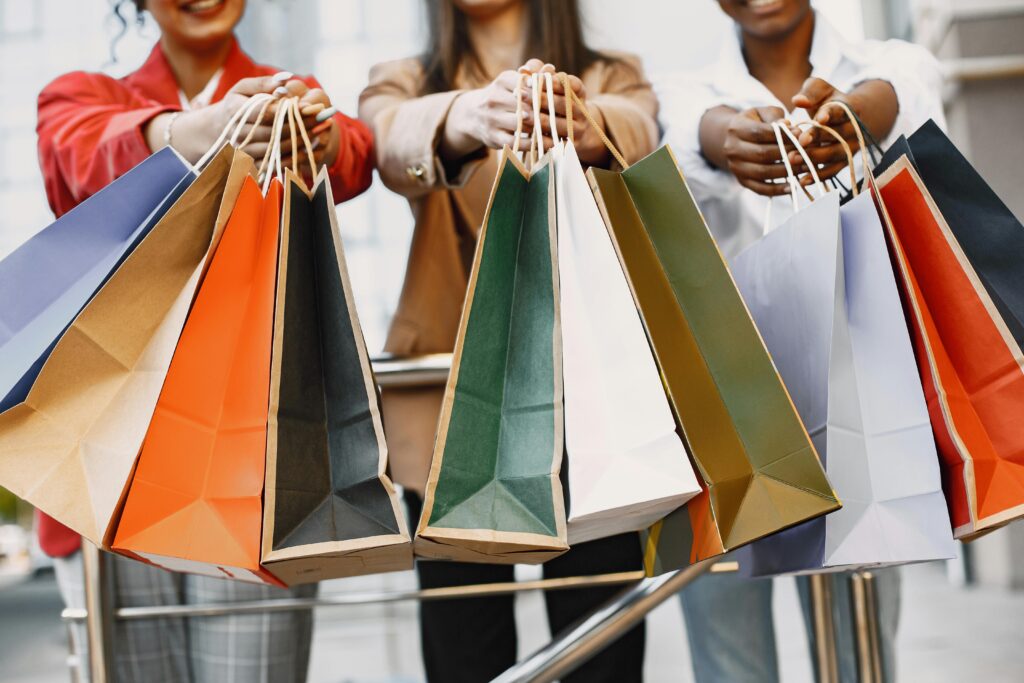 Three women display vibrant shopping bags in an outdoor urban setting, suggestive of a successful shopping spree.